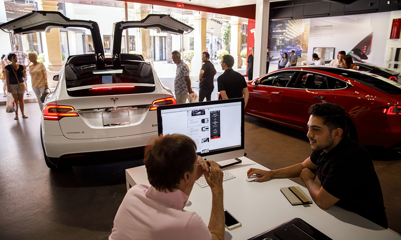 consumers look at a tesla in a tesla showroom