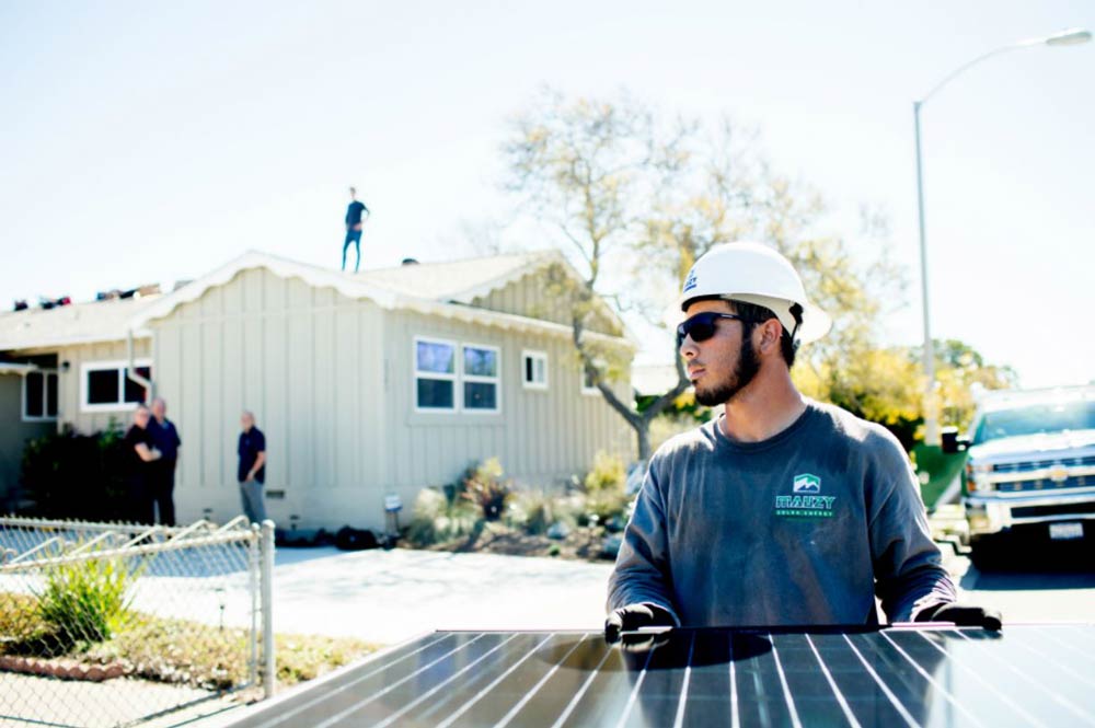 a solar installer carrying a solar panel towards a home